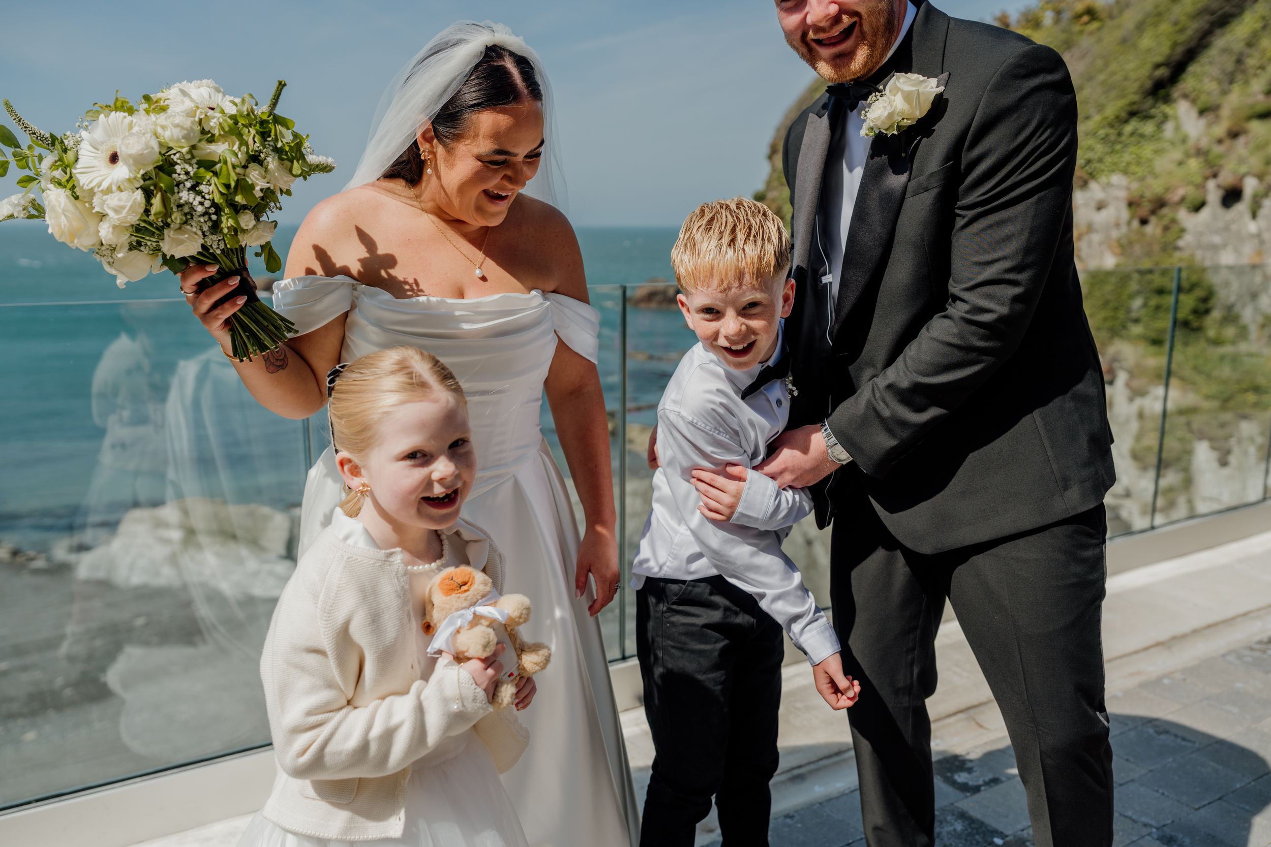 Happy bride and groom with two young children celebrating after their seaside wedding ceremony.