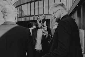 Black and white photo of stylish groomsmen in tuxedos socializing at wedding.
