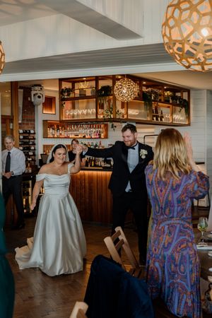Bride and groom make a grand entrance into their wedding reception at a stylish restaurant venue.