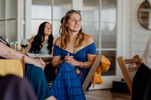 Smiling woman in blue off-shoulder dress enjoys conversation at an outdoor wedding reception.