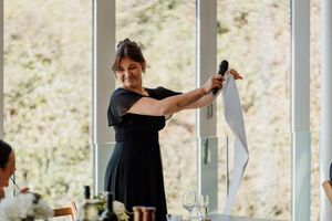 Woman in black dress giving a speech while holding a microphone and paper at a wedding reception.
