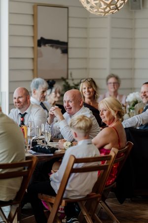 Wedding guests laughing and enjoying conversation at rustic wooden tables during a warm indoor reception.