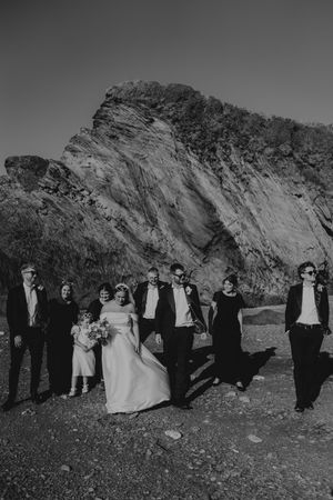 Black and white photo of wedding party walking together in front of dramatic rocky cliff landscape.