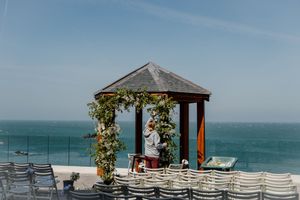 Outdoor wedding ceremony gazebo adorned with flowers overlooking a stunning ocean backdrop.