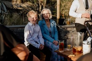 Joyful young boy and elderly woman laughing together at an outdoor wedding reception celebration.