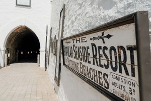 Vintage sign for The Popular Seaside Resort at Frinton Beaches displayed on a white stone wall.