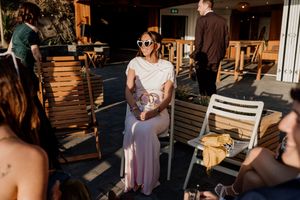 Wedding guest in white top and pink skirt wearing sunglasses relaxing on outdoor patio seating area.
