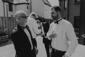 Two men in tuxedos having a conversation outdoors at a wedding preparation.