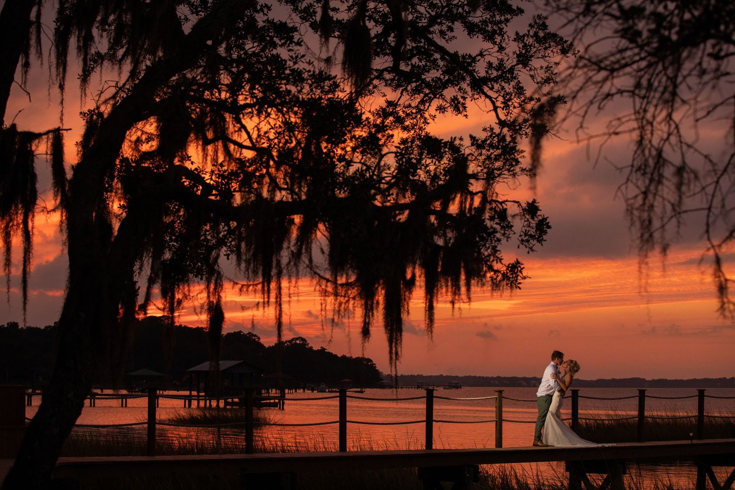 Couple walks beneath massive live oak trees draped in Spanish moss in a lush Southern landscape at golden hour.