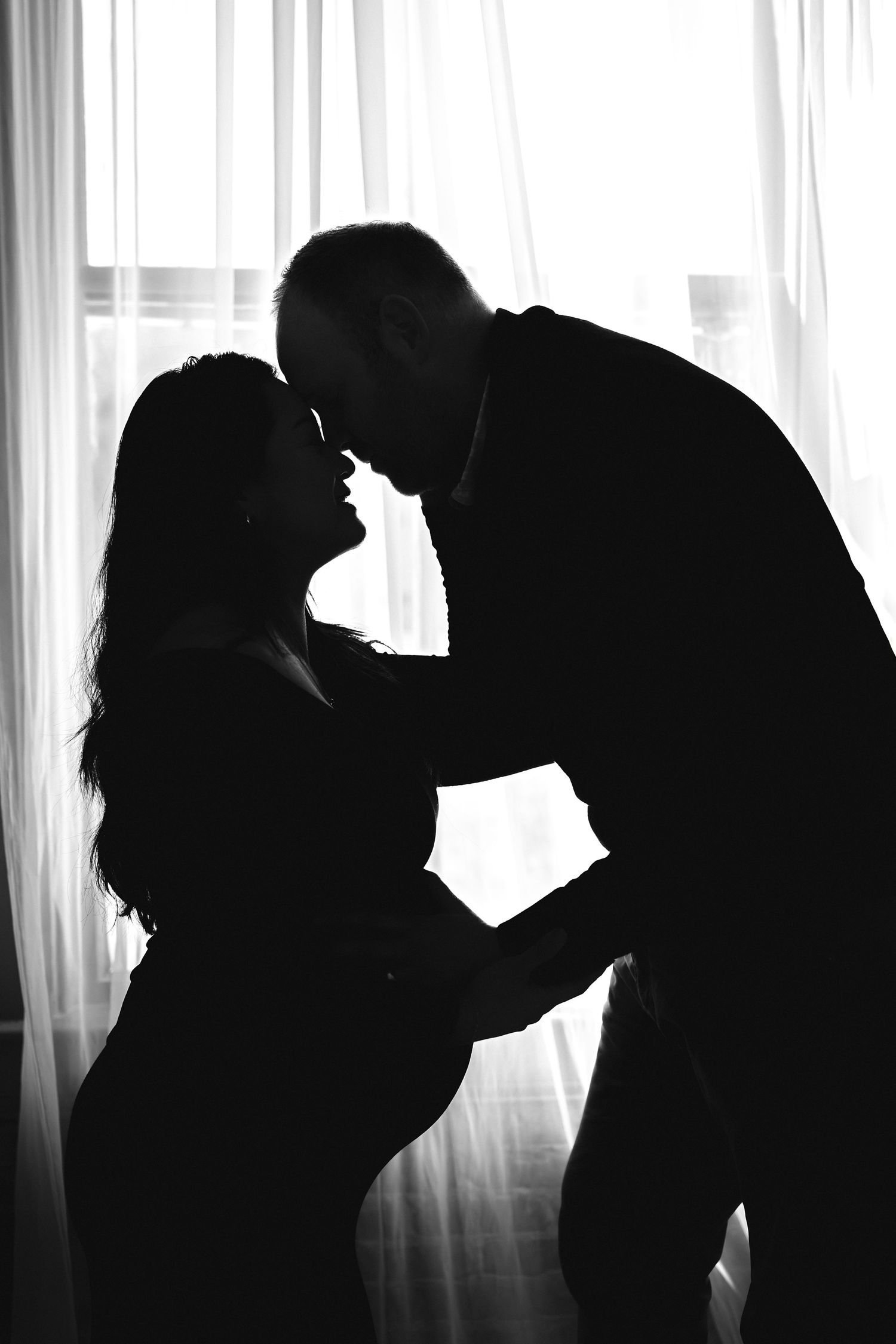 Black and white silhouette of a couple kissing in front of a bright window during maternity photo session with Atlanta maternity photograper