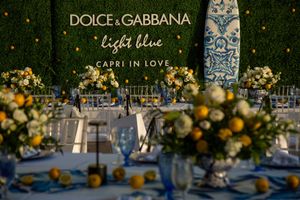 Elegant wedding reception table setting with floral arrangements and Dolce & Gabbana branding against a dark background.
