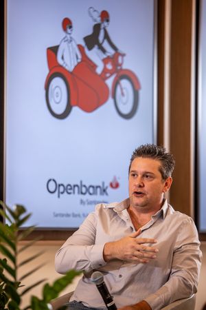A person speaks during a business presentation with an Openbank logo showing a red and white motorcycle illustration behind them.