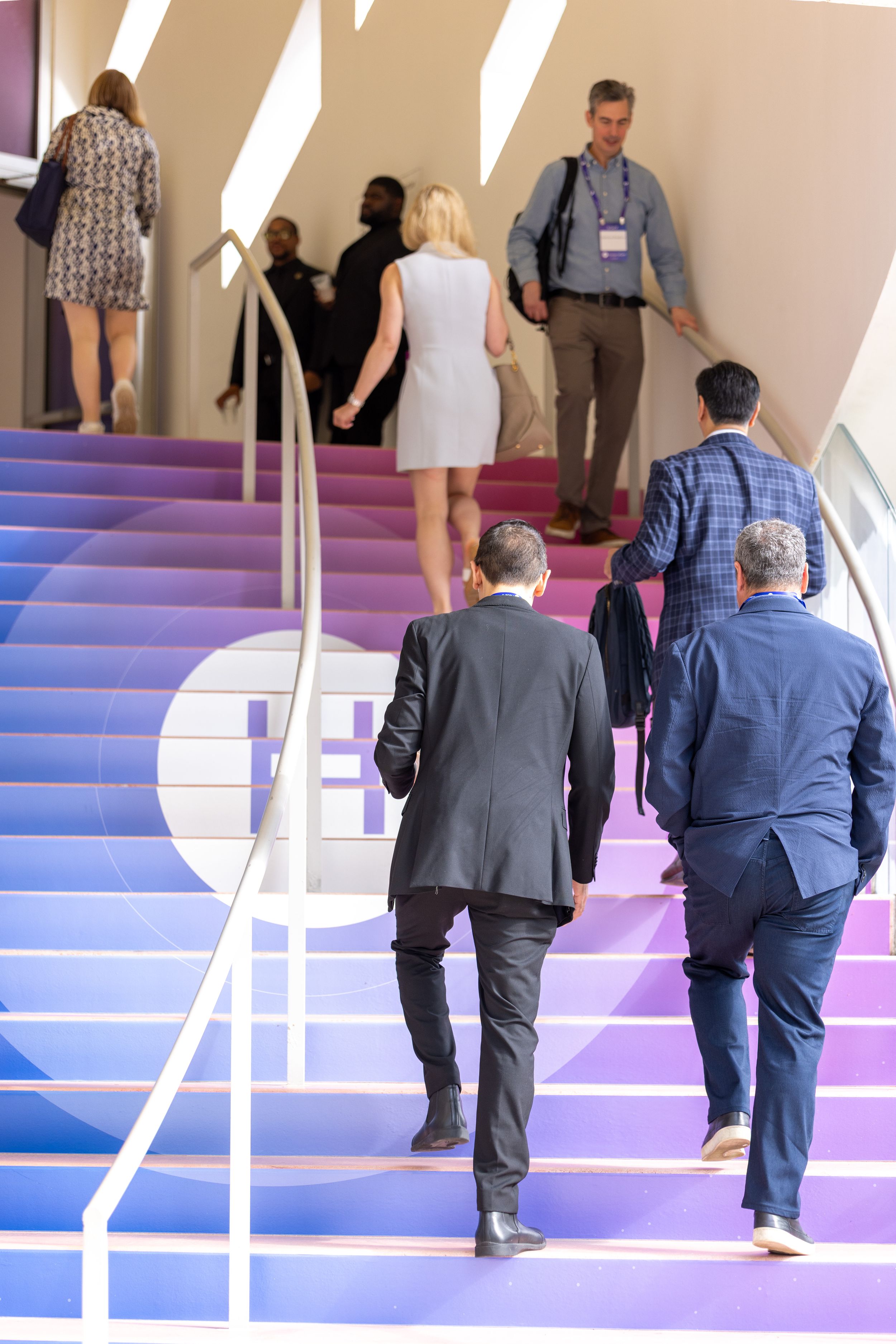 Business professionals walking up colorful purple gradient stairs at a conference event.