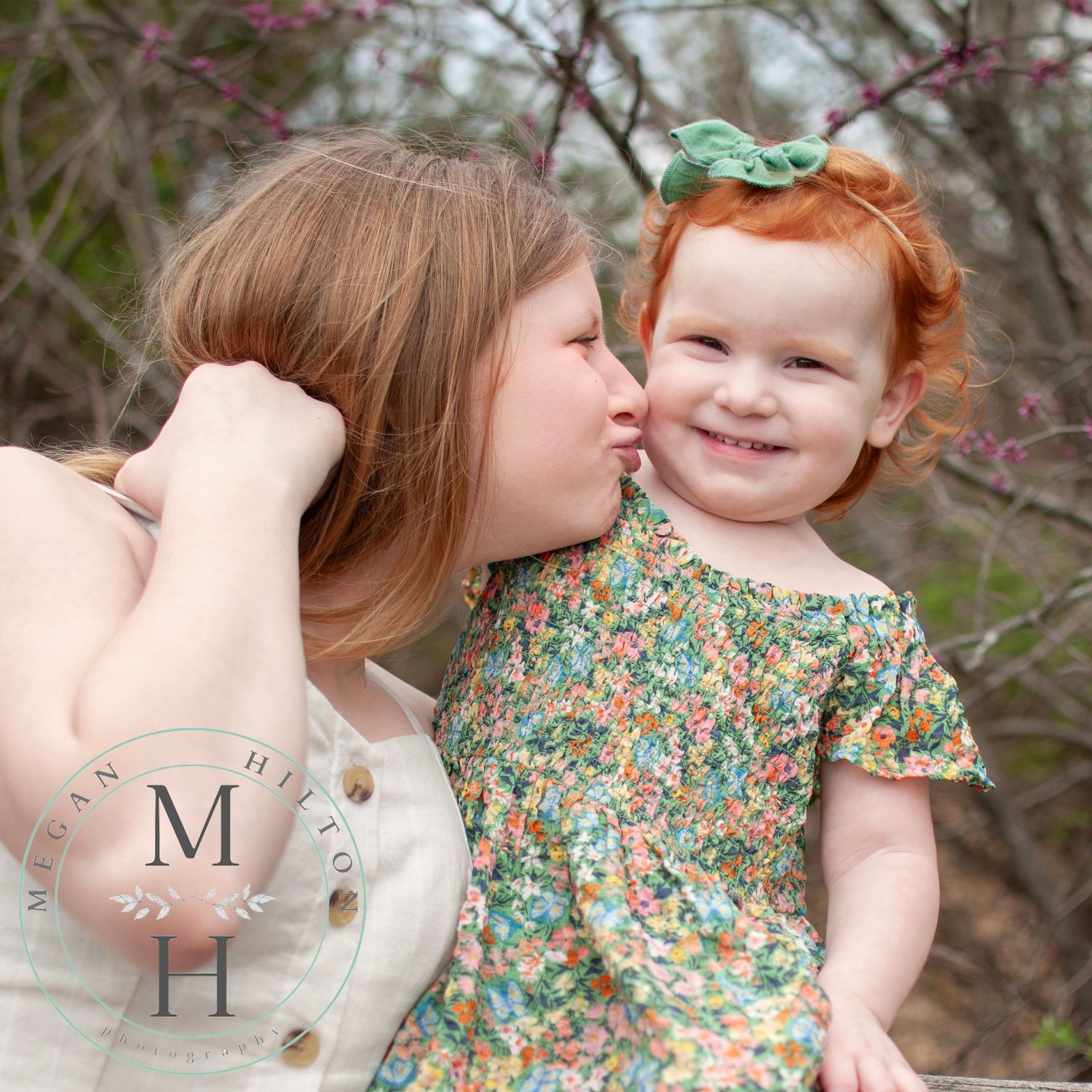 An intimate moment captured outdoors showing a touching expression of love between two sisters wearing floral print dresses.