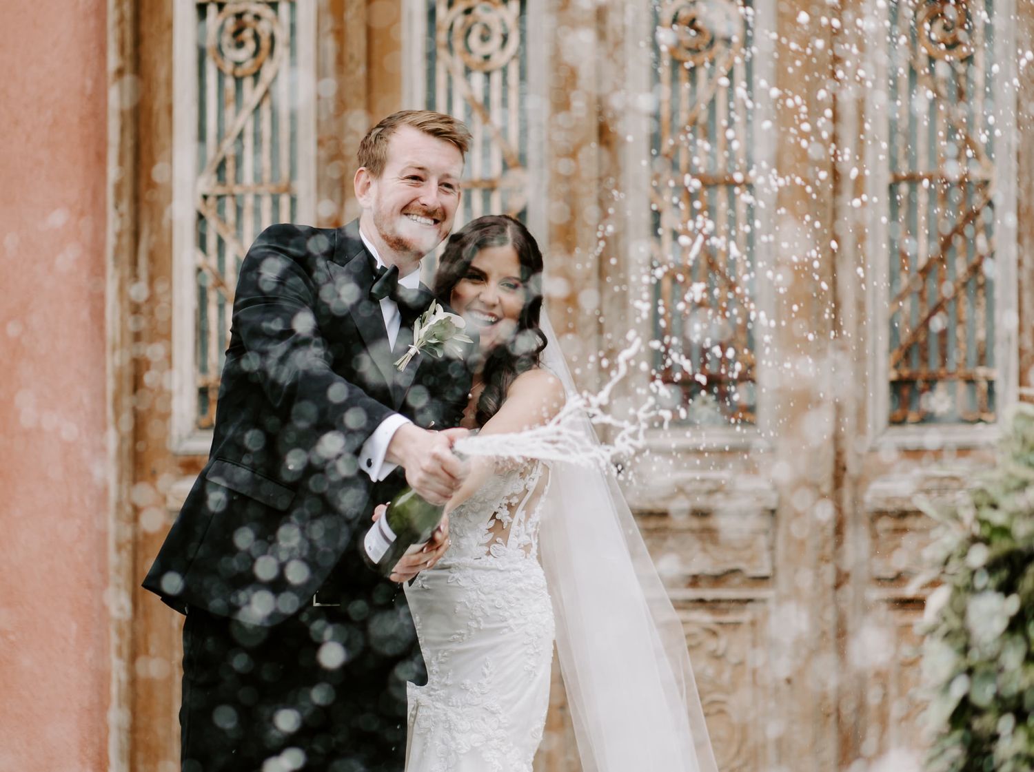 Wedding couple celebrating amid falling confetti in front of ornate building.