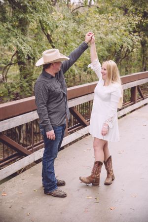 Couple in western wear dancing and twirling on wooden bridge.