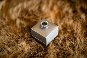A sparkling engagement ring on silver box against brown fur texture.