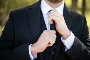 Close-up of hands adjusting a black tie and suit in an outdoor setting.