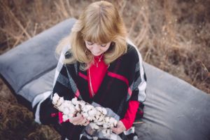 Person in black and red sweater sitting on cushion holding cotton flowers.