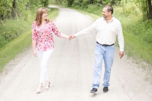 Couple holding hands while walking on rural dirt path surrounded by greenery.