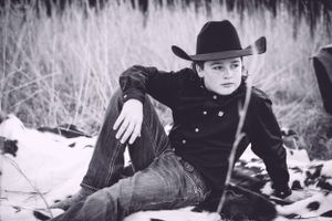 Person in cowboy hat and black outfit reclining on snowy ground in black and white photo.