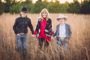 Three people standing together in tall grass field at sunset.