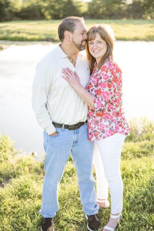 A couple embraces in a sunlit field wearing casual clothing and sharing an intimate moment together.