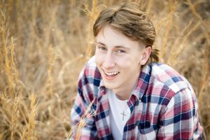 Portrait of someone smiling in a plaid shirt surrounded by tall grass.