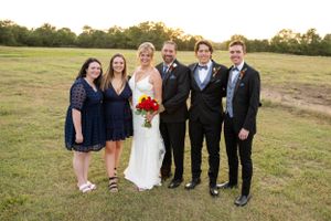 Wedding party group photo outdoors with bridesmaids and groomsmen on grassy field at sunset.