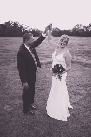 Black and white photo of newlyweds celebrating with raised hands in outdoor field.