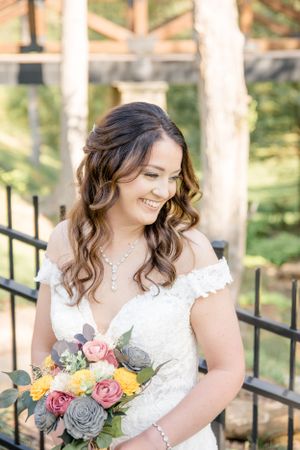 A bride in a white lace dress holds a colorful bouquet with pink and yellow roses and succulent accents.