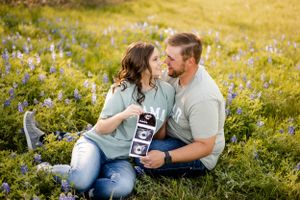 Expecting couple shares intimate moment in wildflower field while holding ultrasound photos.