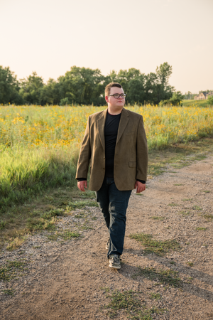 Person in brown blazer walking on path through field of yellow wildflowers at sunset.