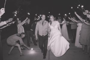 Wedding couple exits through sparkler tunnel during nighttime celebration.