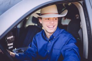 Person in cowboy hat and blue shirt sits in driver's seat of car.
