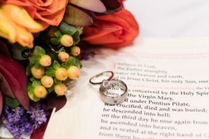 Wedding rings and colorful flowers rest on an open Bible verse.
