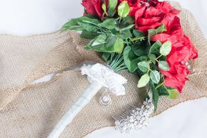 Wedding accessories with red roses and lace details on burlap.