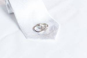 Wedding rings resting on a white silk tie in a close-up detail shot.