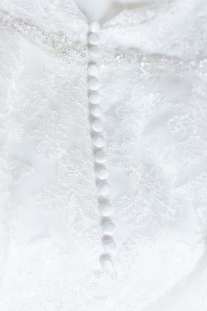 Close-up detail of delicate white wedding dress buttons and lace.