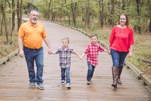 Family of four walking together on wooden boardwalk through wooded area.