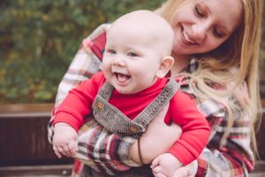 Baby in red outfit and overalls laughing while being held.