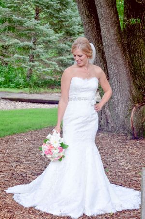 Bride in fitted lace wedding gown poses by tree in garden setting.