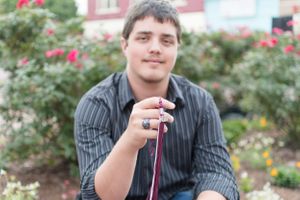 A casual portrait in front of flowering bushes with someone holding earbuds outdoors.