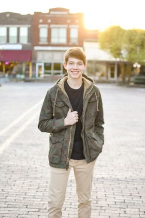 A casual portrait of someone in an olive jacket standing on cobblestone at sunset.