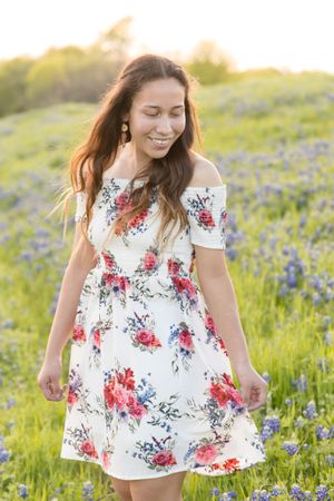 A woman in a floral dress stands among bluebonnets at sunset.