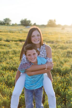 A playful piggyback pose captured in a sunny meadow at golden hour.