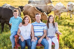 A family sits on wooden benches in a pasture with cattle grazing behind them.