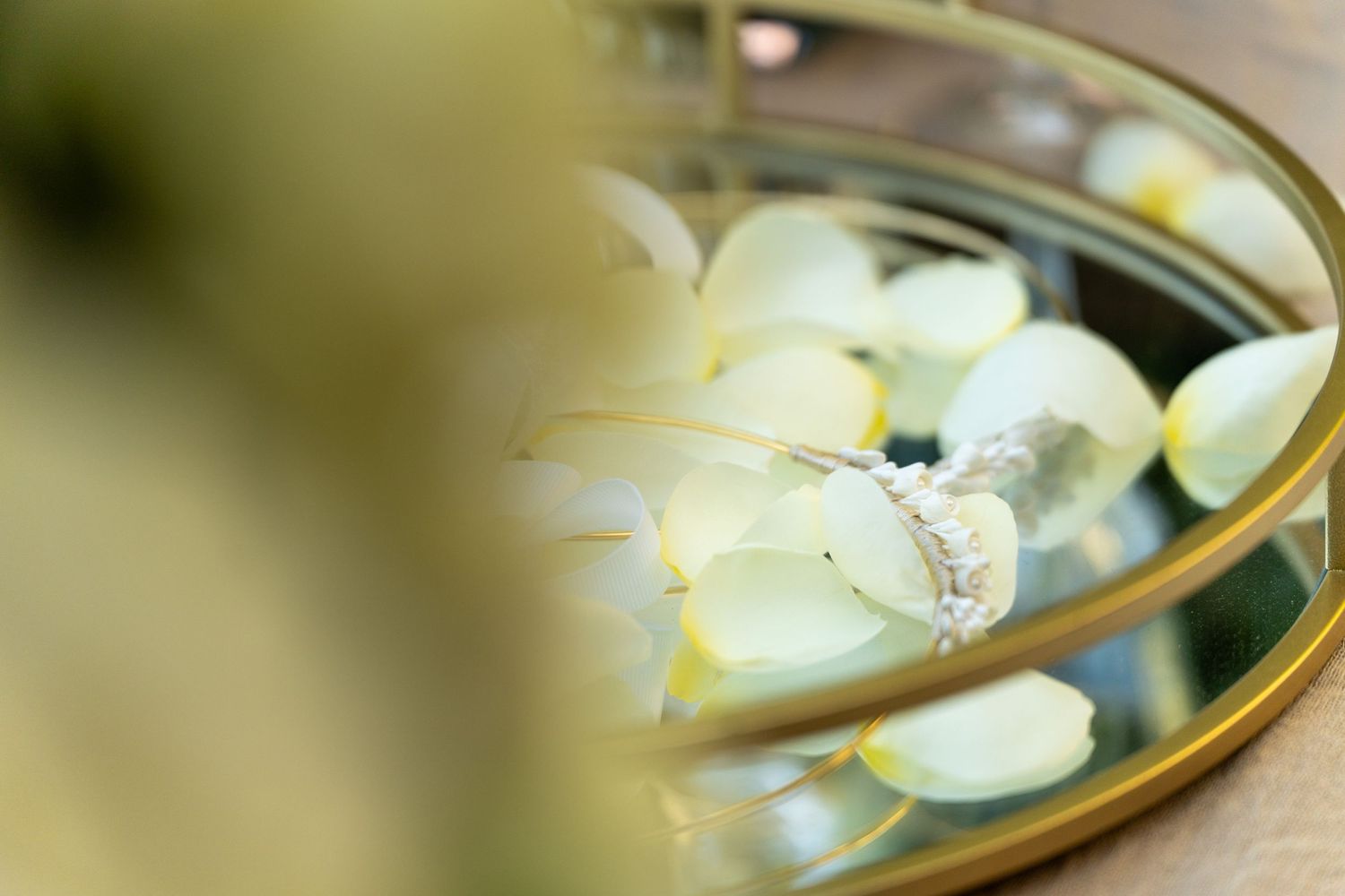 Wedding rings reflected in mirror with soft focus white flower petals in background.