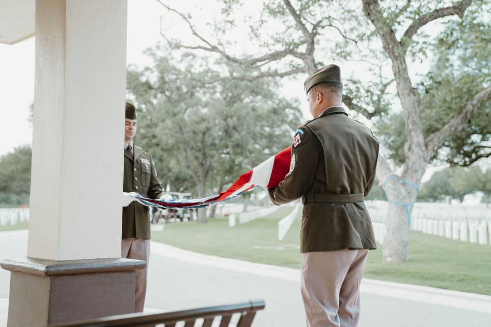 Two military officers in uniform folding an American flag during a ceremonial service at a national cemetery.