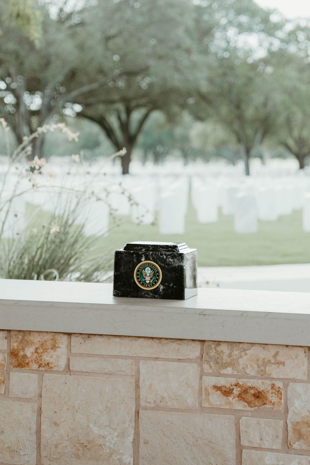 Military urn on stone ledge at a national cemetery with white grave markers visible in background.